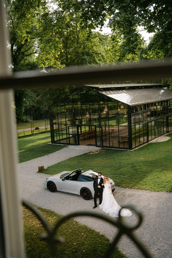 Brautpaar am Sportwagen vor der gläsernen Orangerie im Schlossgut Lautenbach