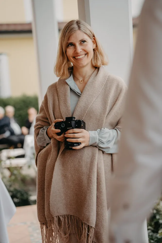 Lisa lächelt mit der Kamera in der Hand bei einer Trauung