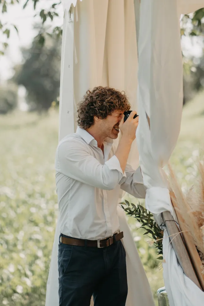Stephan fotografiert lachend zwischen den Vorhängen einer freien Trauung